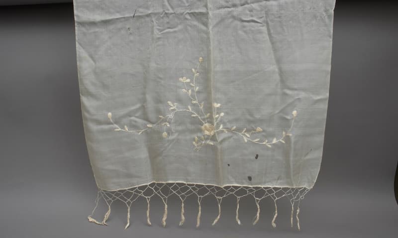 A delicate white silk scarf with a fringe and embroidered flowers and leaves