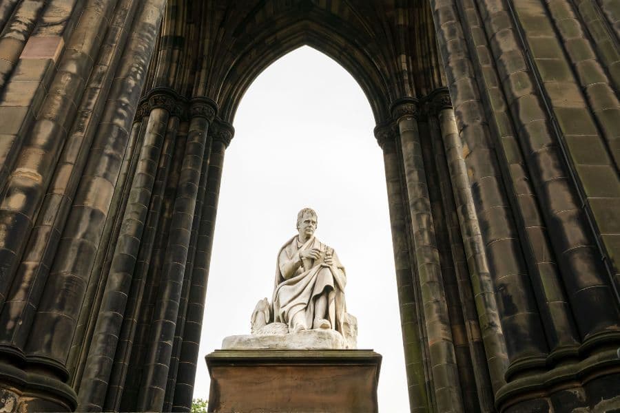 Image of a white marble statue of a man sitting at the foot of a monument