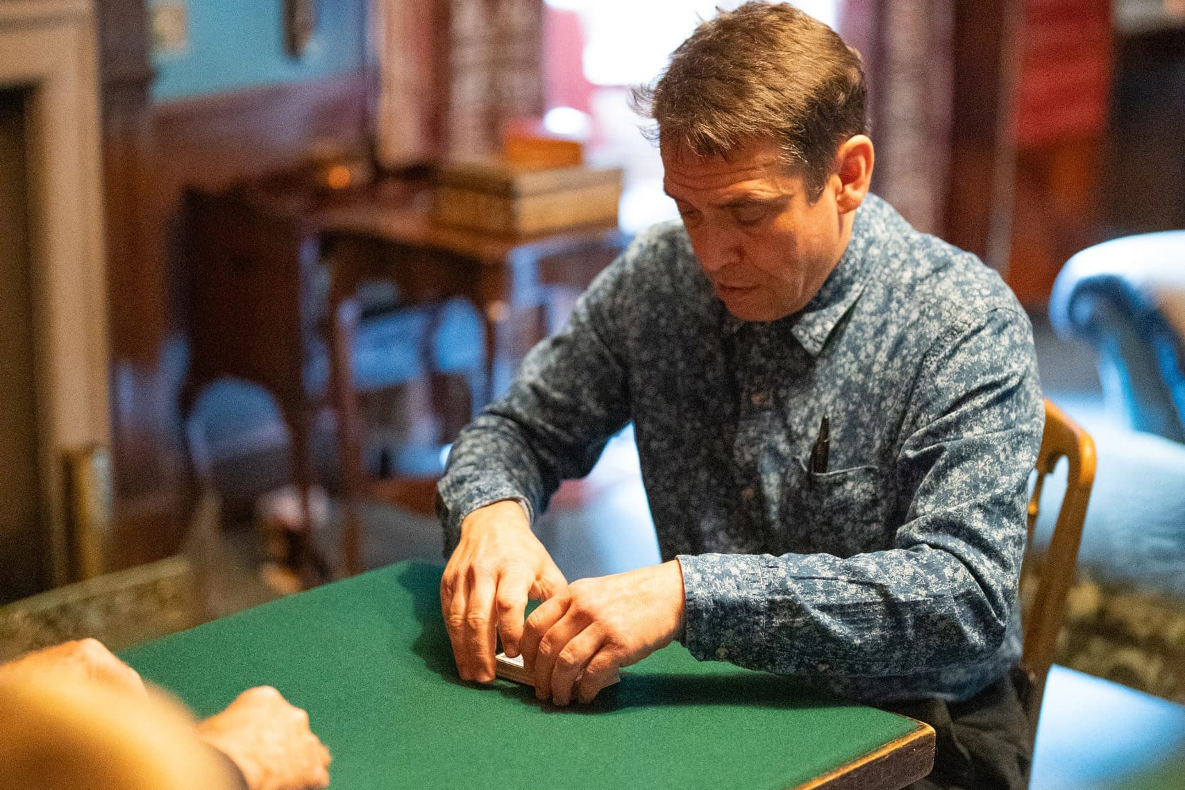 A man sits engaged at a table with a green cloth and focused on a deck of cards.