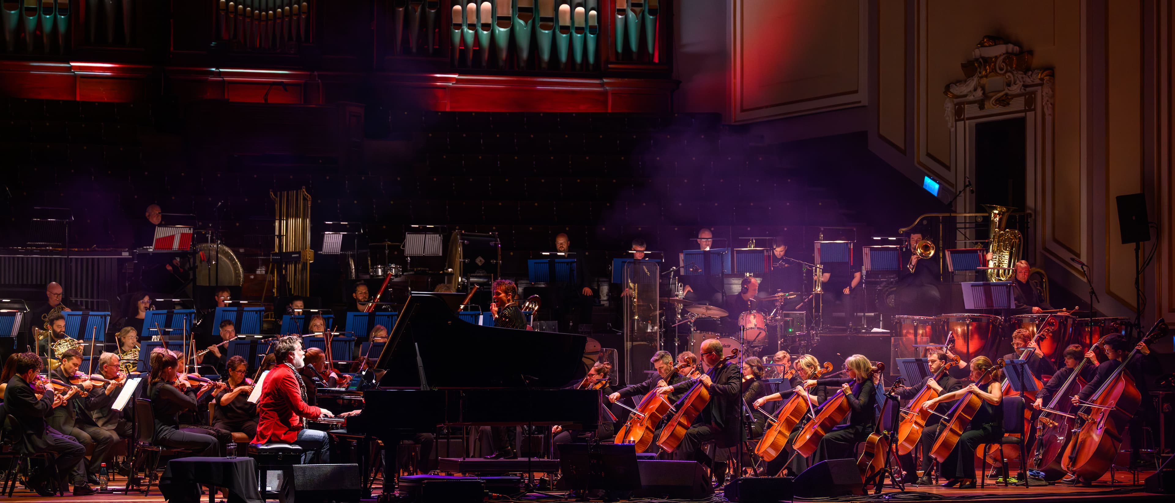 A colourful concert with an orchestra and a person on a piano signing.
