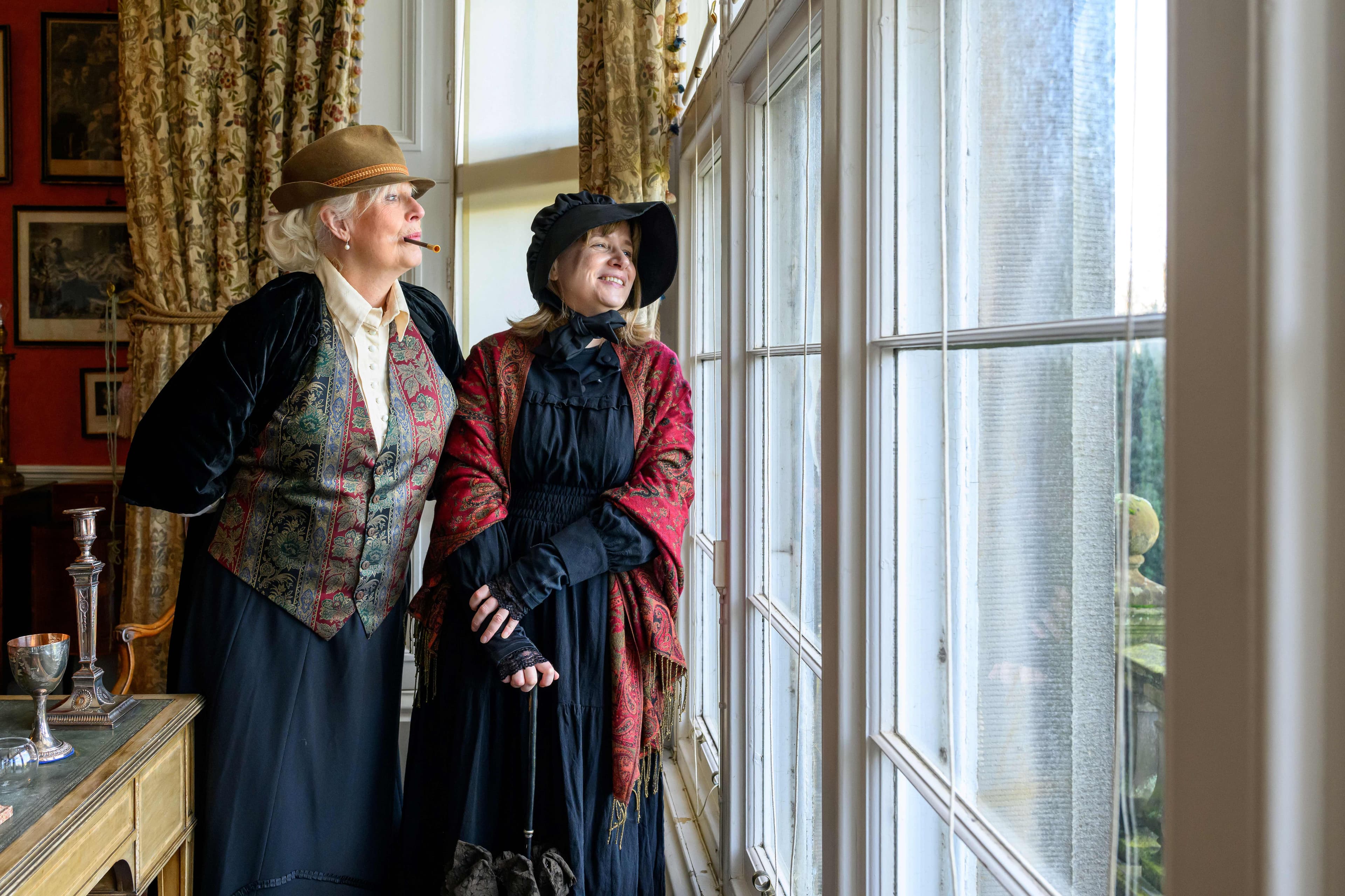 Two women in period costume looking out of a window