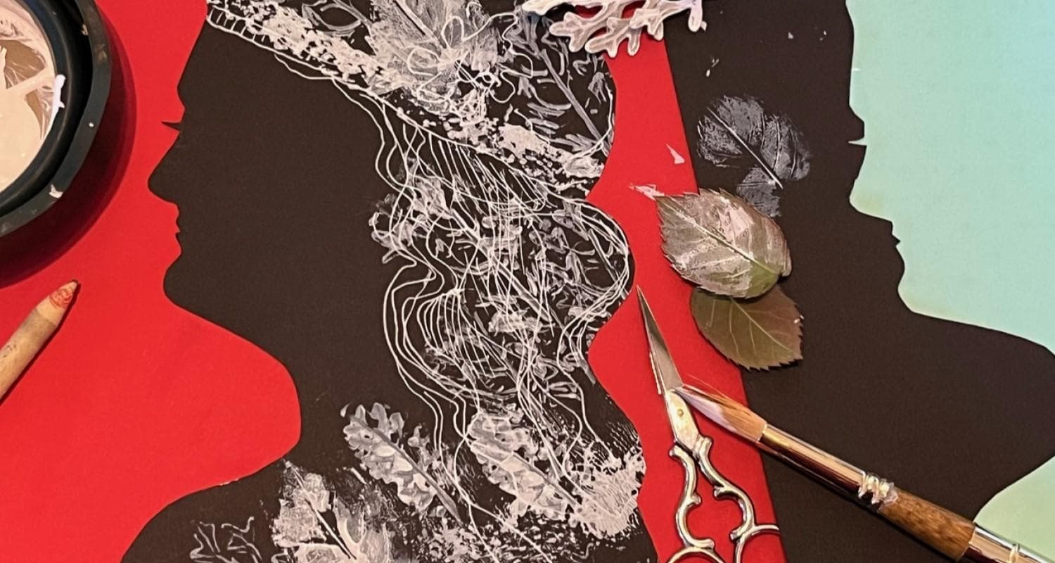 A silhouette of a paper face on red craft paper surrounded by a pair of scissors, pencil, paint brush and leaves 