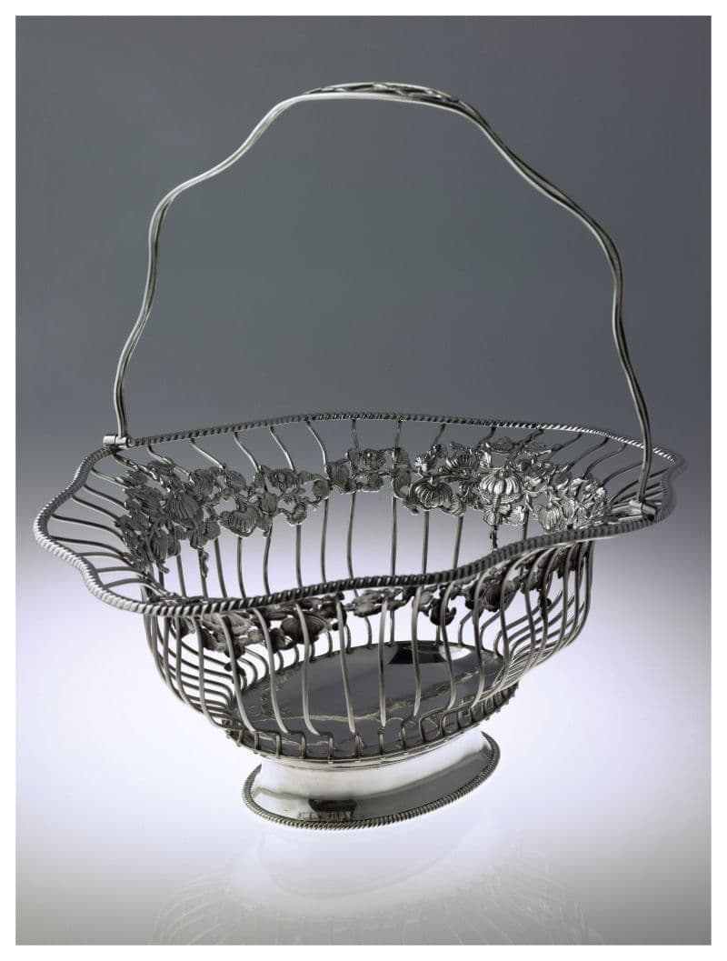 A silver basket featuring a curved handle and decorative flowers