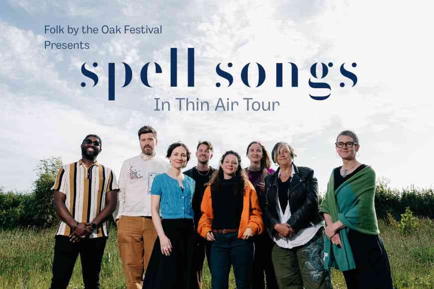 Spell songs band members stood smiling in a field with clouds in the sky