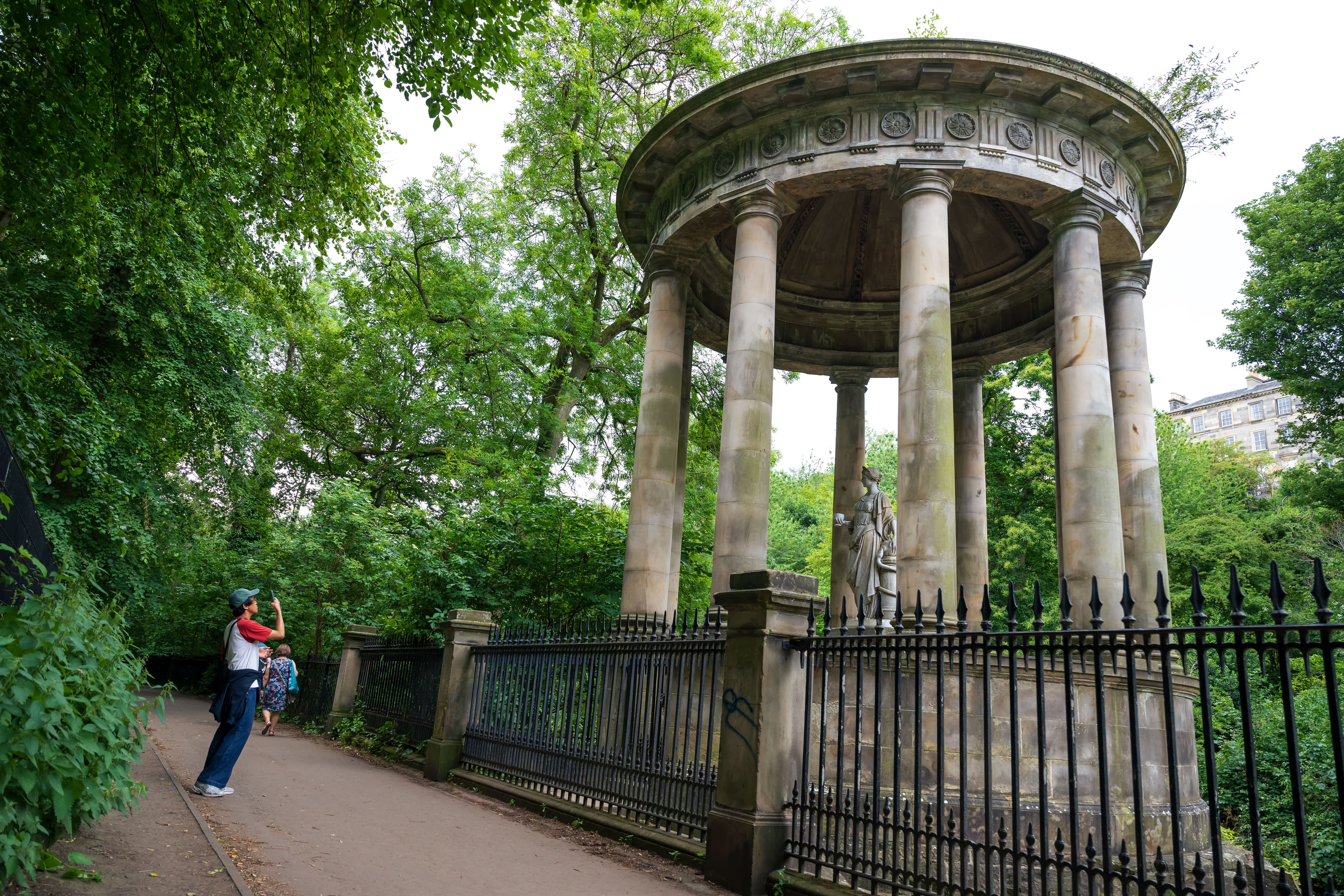 A man taking a photo of a monument nestled in a park landscape.