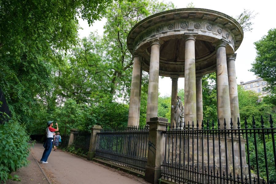 A man taking a photo of a monument nestled in a park landscape.