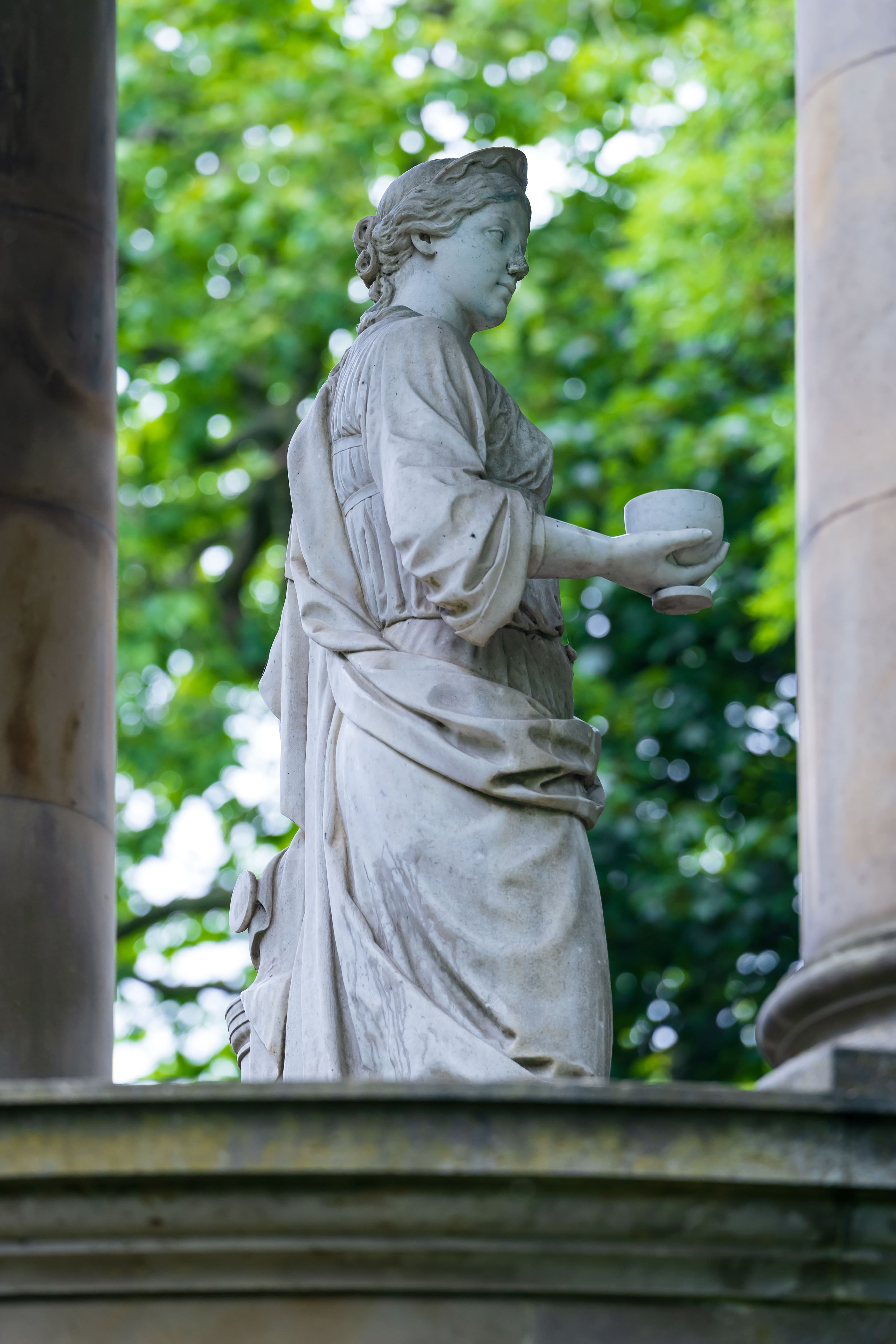 A statue of a woman gracefully holding a cup, symbolizing elegance and poise in a serene setting.