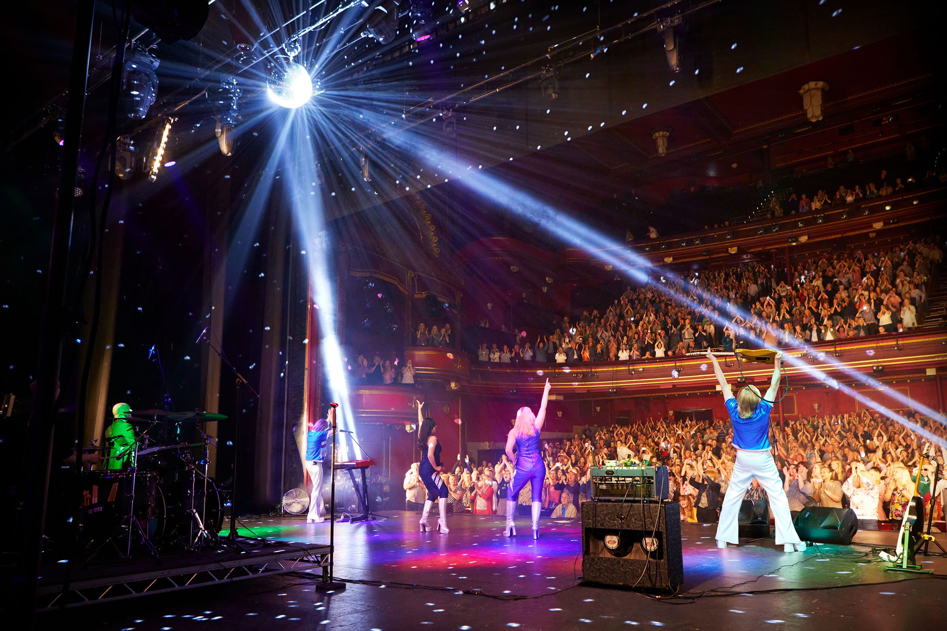A band performs on stage with vibrant lights, while an enthusiastic crowd enjoys the live music experience.