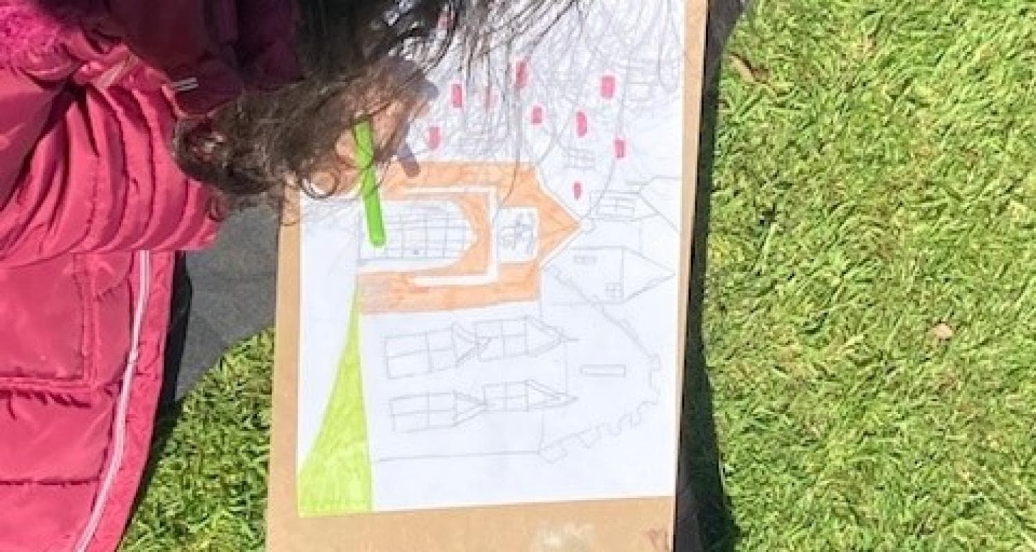 A child focused on drawing on a piece of paper with coloured pencils in the grounds of Lauriston Castle.