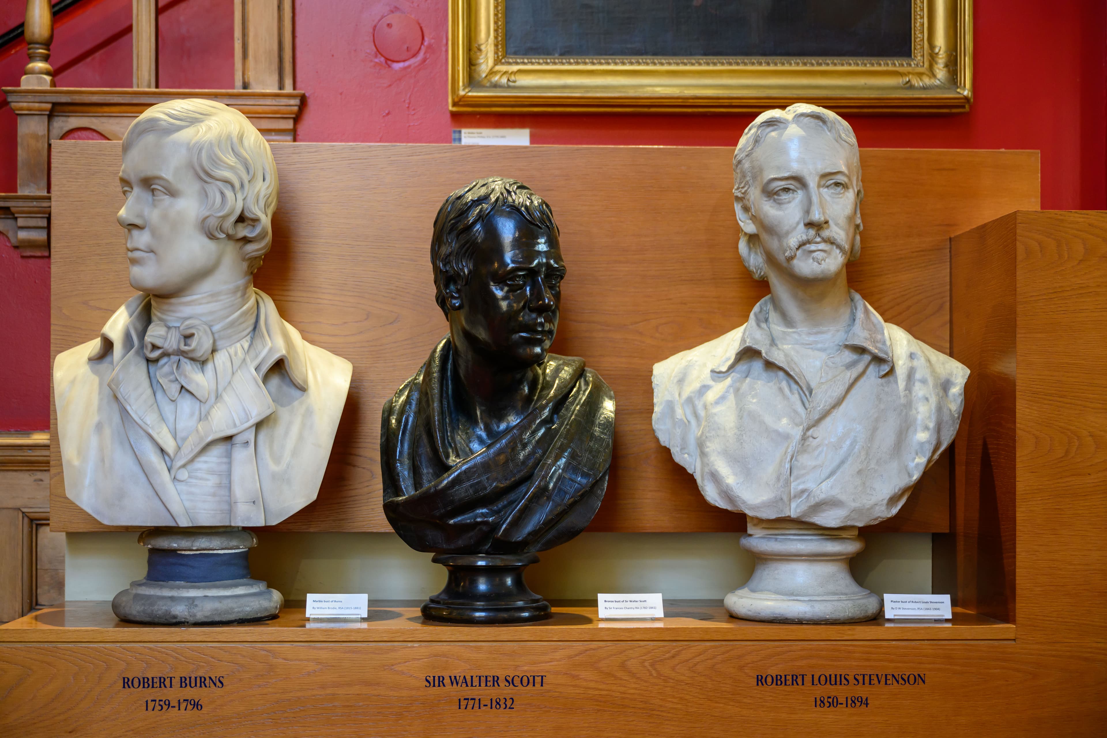 Three marble busts of men displayed on a wooden shelf, showcasing intricate details and expressions.