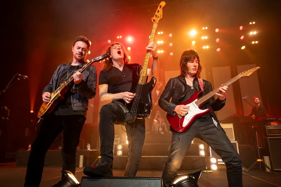 Image shows 3 men on stage playing guitars