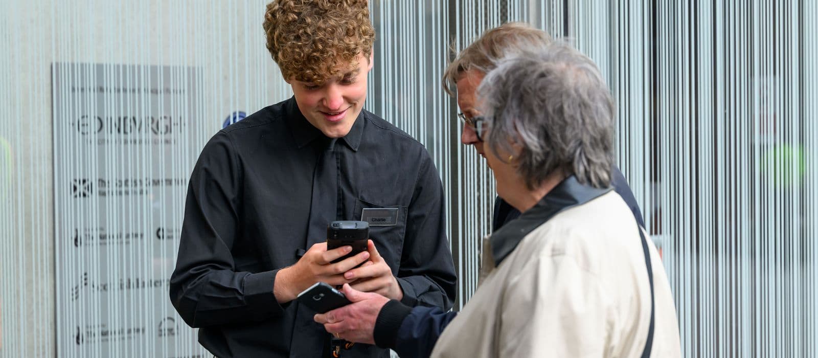 A Usher Hall staff member in a black shirt engages in conversation with two customers about tickets.
