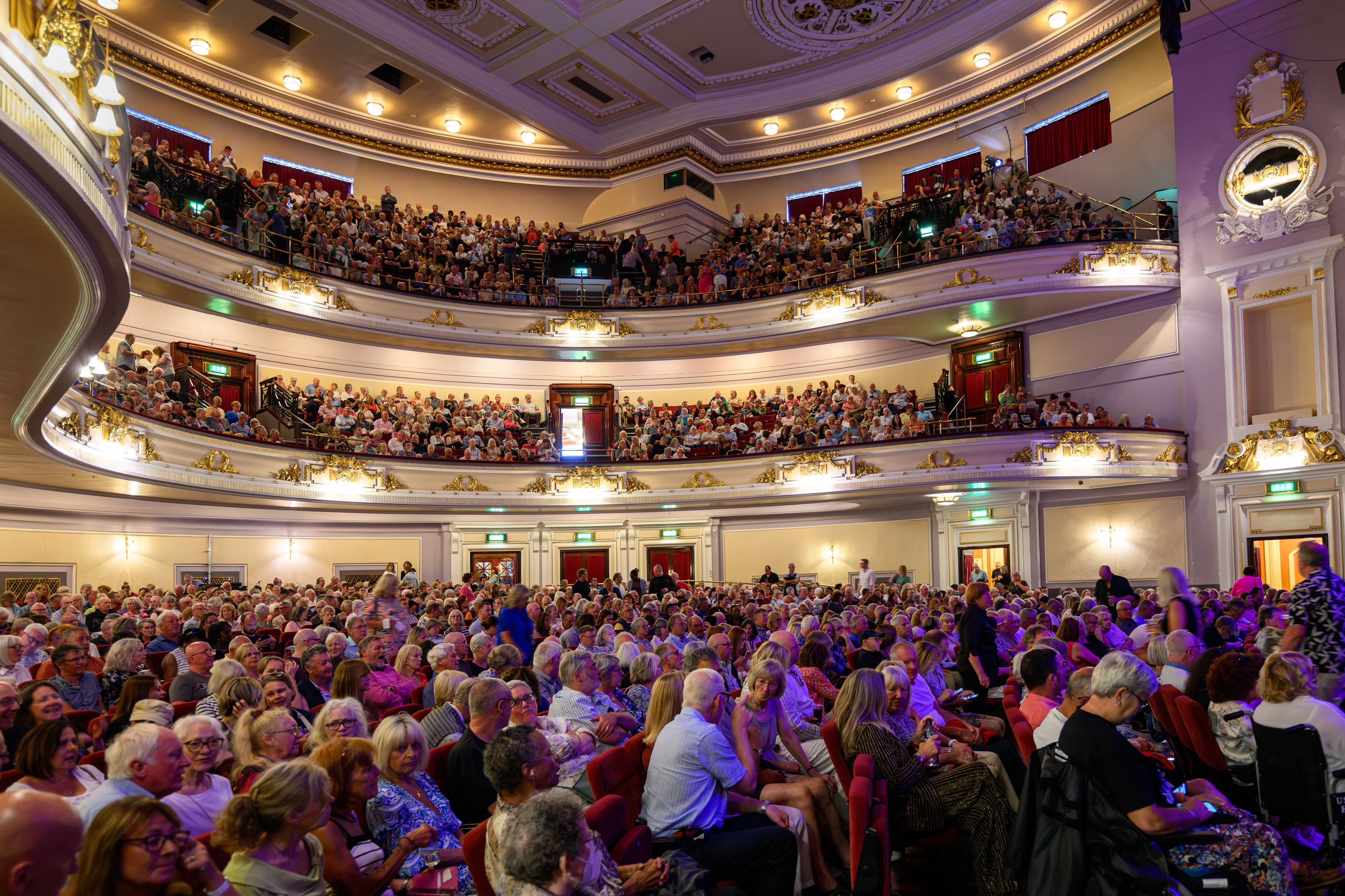 A wide view of a crowded auditorium, showcasing numerous people seated and participating in an event.