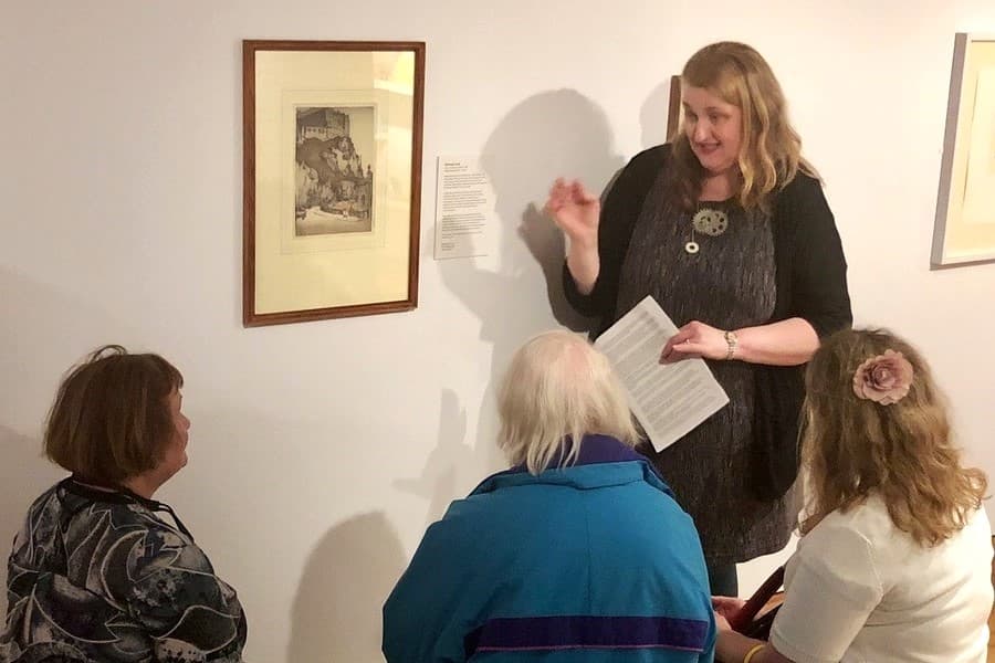 Visually impaired people seated in front of artwork. A guide describes the artwork.