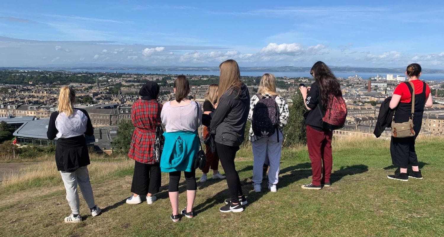 A group of young people stand on a hill overlooking Edinburgh