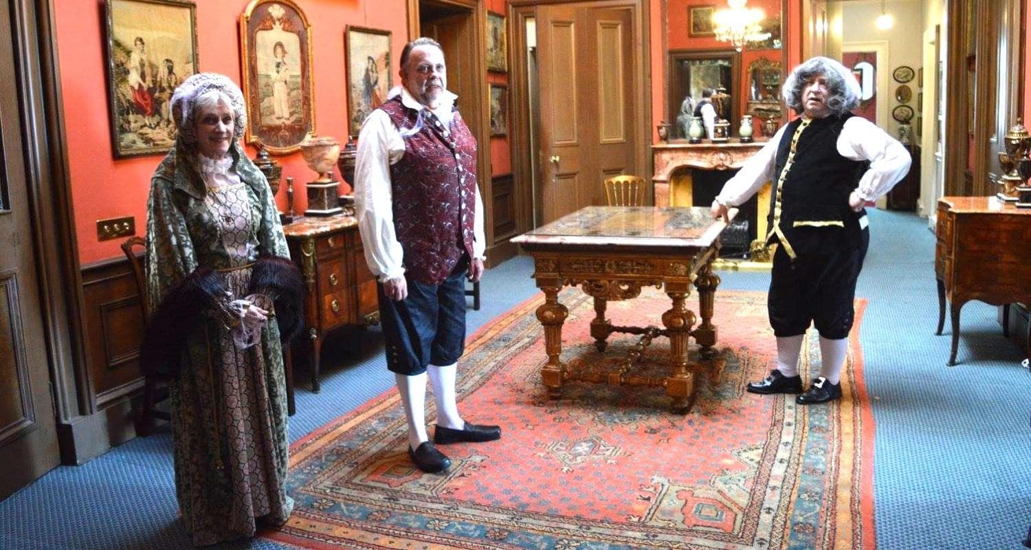 Three individuals dressed in Edwardian costume and stand together in the hall of Lauriston Castle