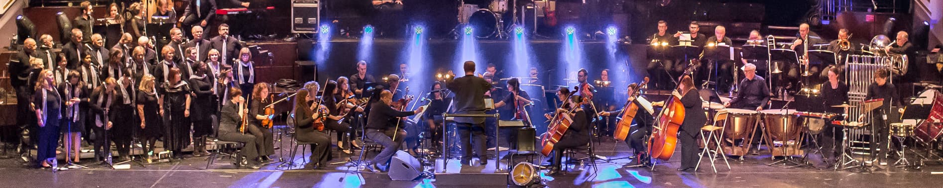 A conductor directs an orchestra and choir on stage 