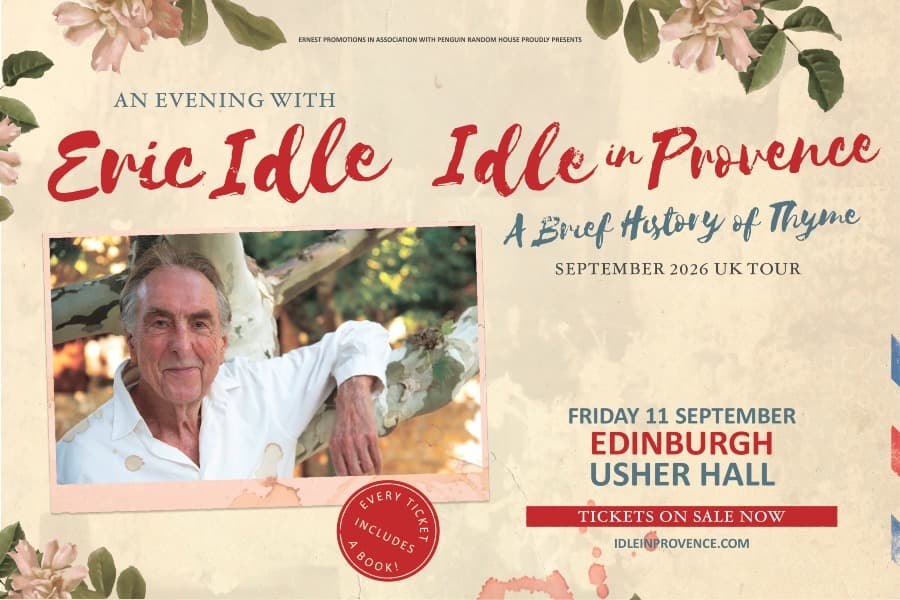 Image shows Eric Idle posing beside a tree