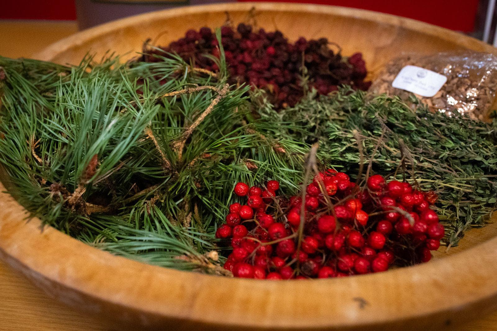 A wooden bowl containing winter berries and fir tree branches