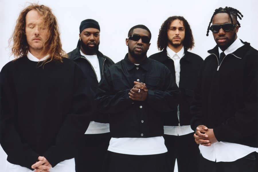 Photograph of Ezra Collective band members all wearing either a black jacket or jumper over a white shirt or T-shirt and black jeans