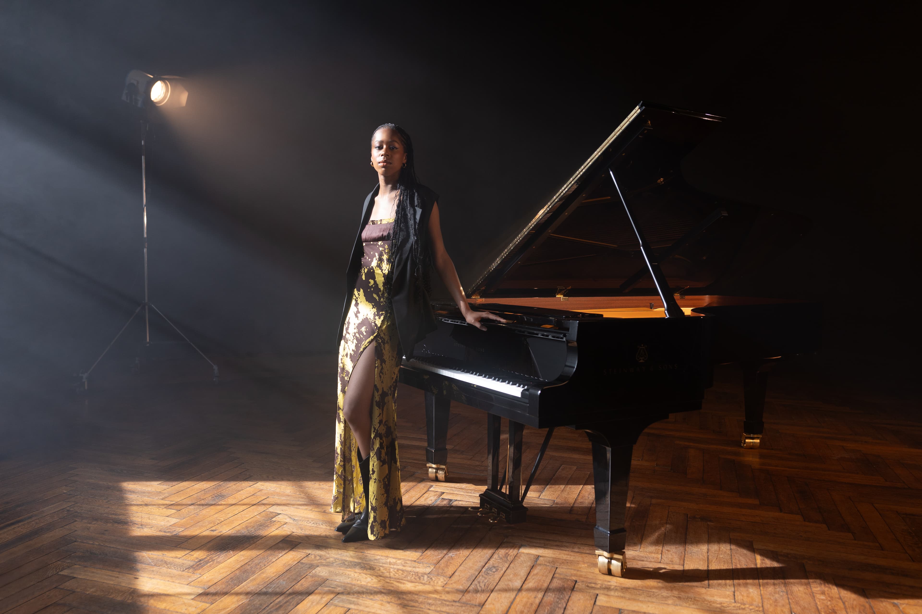 Jeneba Kanneh-Mason stood in front of a piano wearing a long grey and green dress.