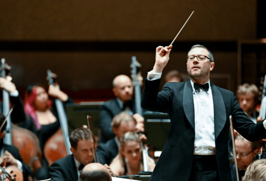 Image of conductor on stage with orchestra