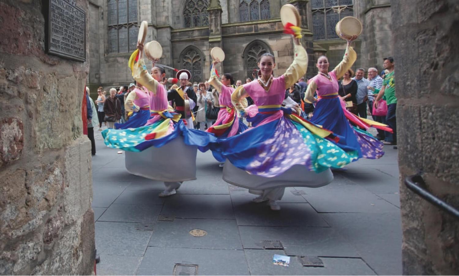 Five dancers in full skirts and with tambourines perform for a crowd on the Royal Mile at the Edinburgh Festival Fringe