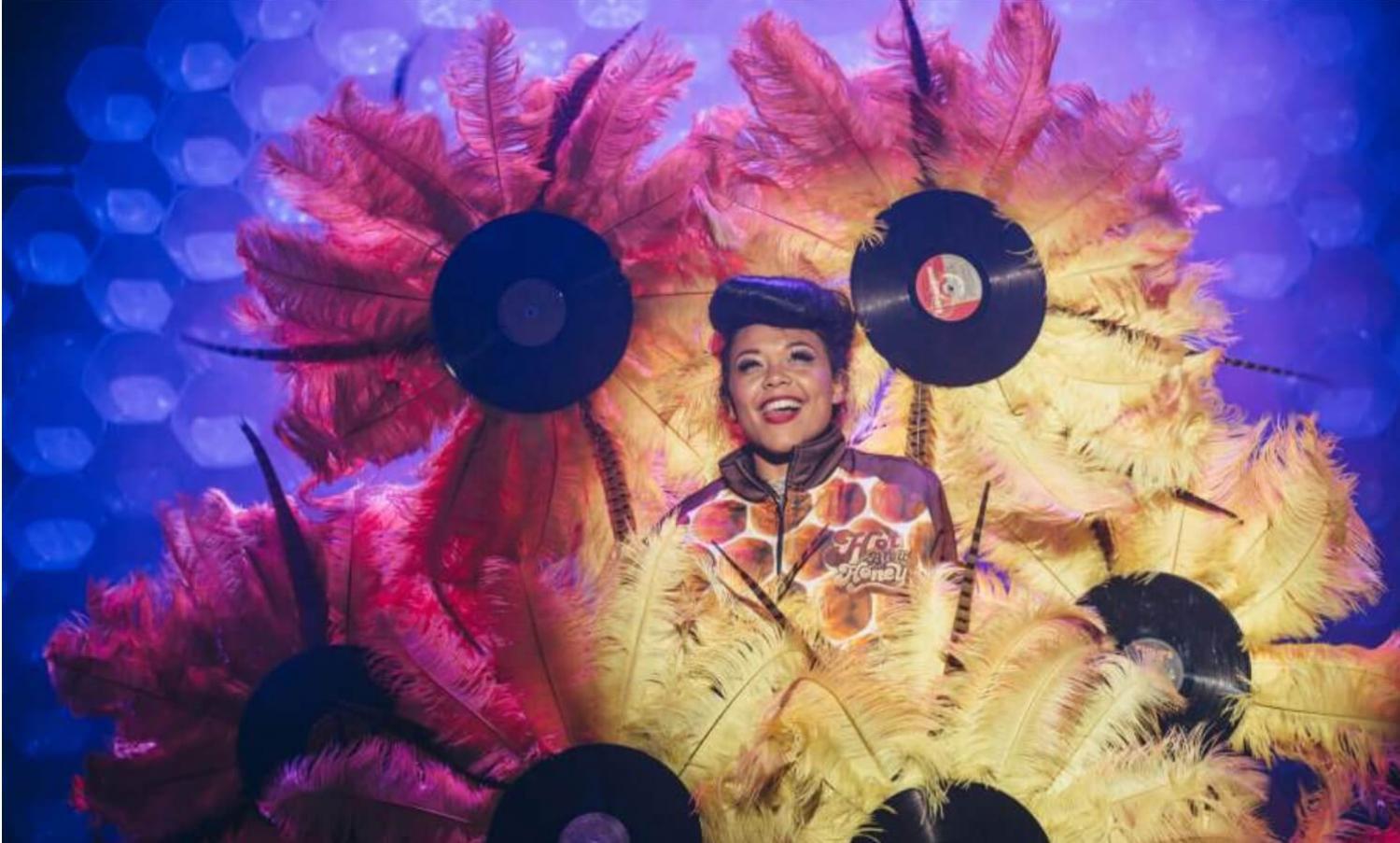 Hot Brown Honey on stage at a Fringe venue surrounded by large feathers and records made to look like flowers. Image by: David Monteith Hodge