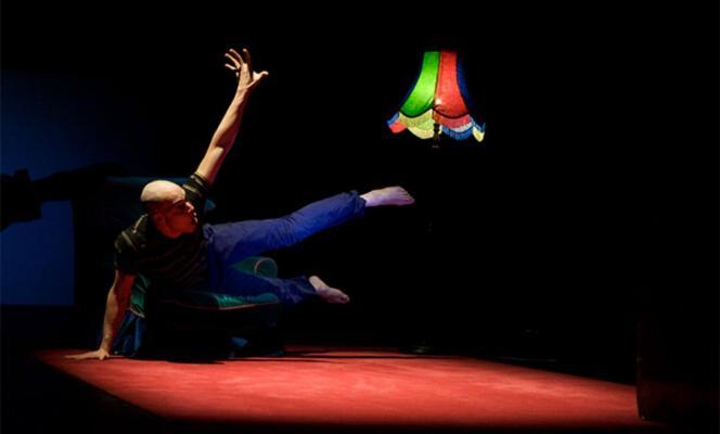 Award Recipient Tony Mills in Watch iT! leaping over props on black stage with a colourful lamp in the background
